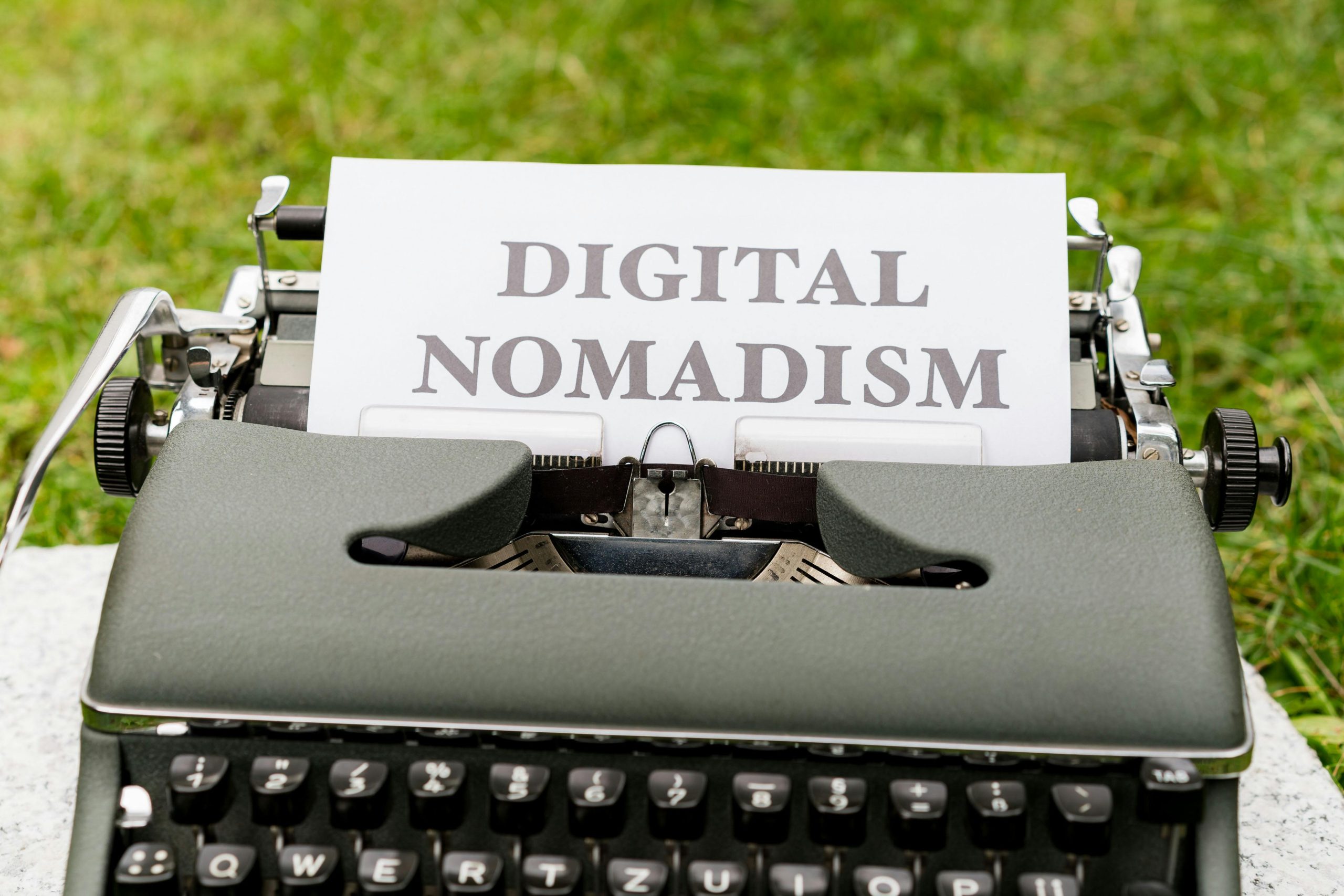 A retro typewriter outdoors with paper showing ‘Digital Nomadism,’ symbolizing flexible work and lifestyle