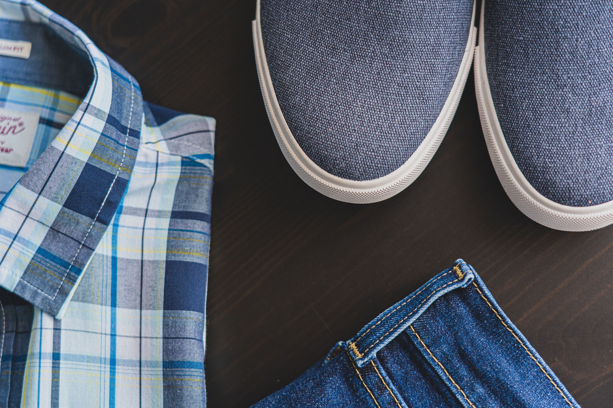 Flat lay of a casual men’s outfit with checkered shirt, denim jeans, and blue sneakers